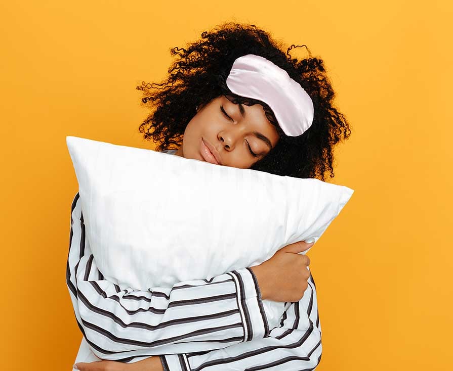 Sleeping. Dreams. Woman portrait. Afro American girl in pajama is hugging a pillow, on a yellow background